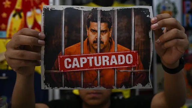 Persona sosteniendo una imagen de Maduro tras las rejas y un sello de "capturado"