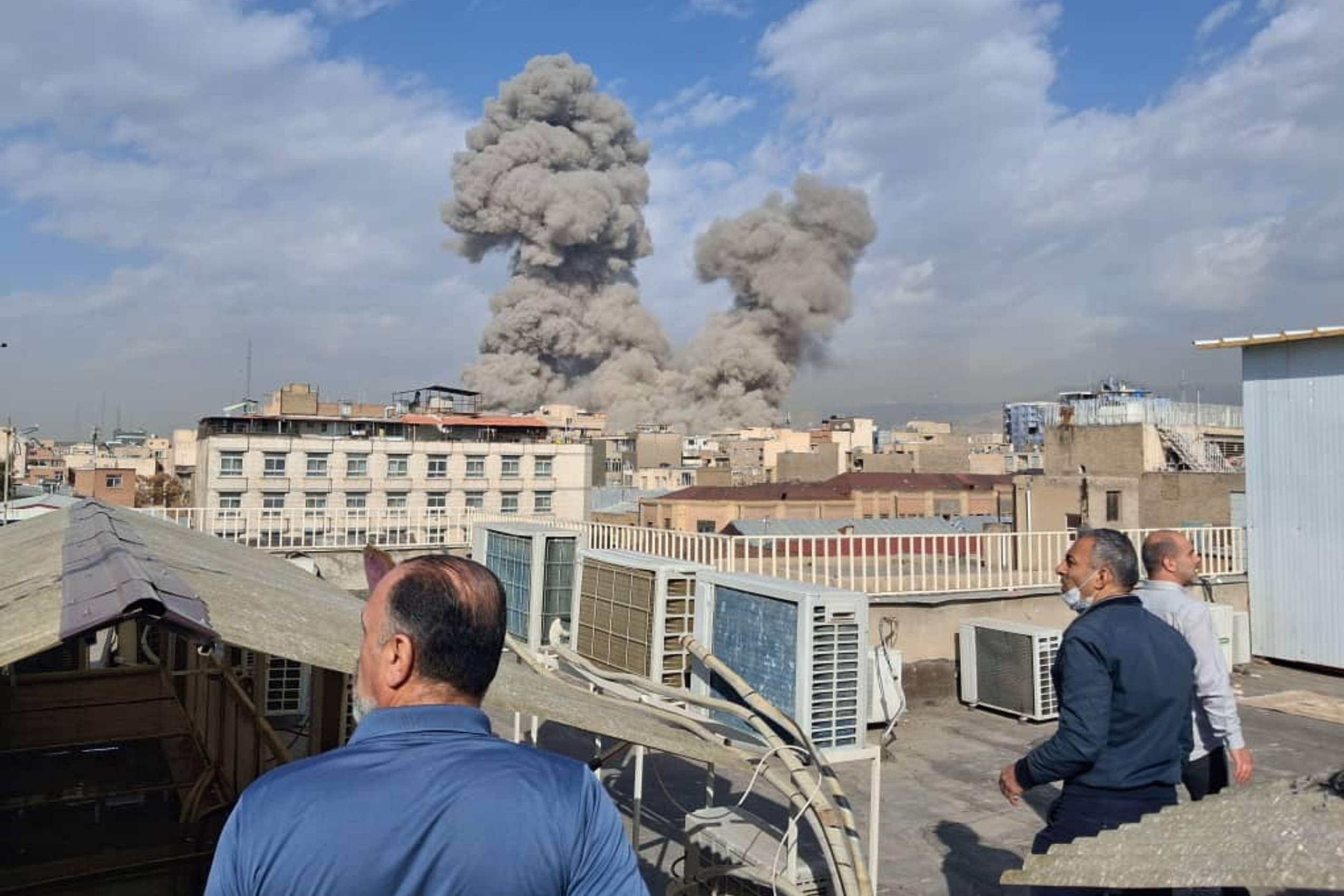 La gente observa una columna de humo después de una explosión en Teherán