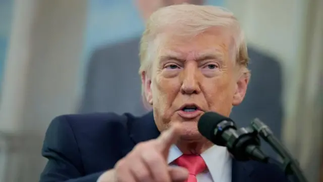 El presidente estadounidense Donald Trump, vestido con traje y corbata roja, señala con un dedo mientras habla por el micrófono.