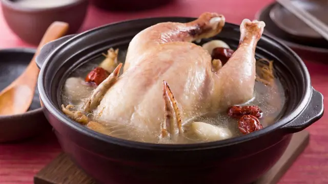 Pollo entero cocido en una olla de barro con caldo, dátiles rojos y ajo.