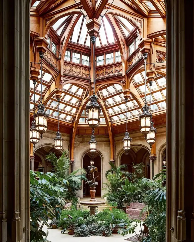 El jardín de invierno de Biltmore House, con altos techos abovedados de madera y vidrio, y palmeras y otras plantas en macetas.
