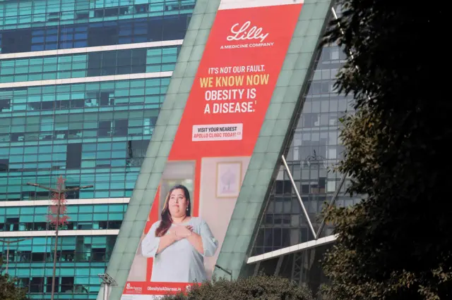 Una valla publicitaria de Eli Lilly en un edificio en Gurugram, India, muestra a una mujer con una túnica y las manos sobre el corazón. El eslogan dice: «No es culpa nuestra. Ahora sabemos que la obesidad es una enfermedad».