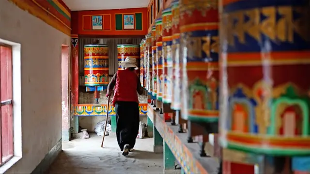 Una mujer camina junto a coloridas ruedas de oración que representan murales de la vida de Buda dentro del monasterio de Kirti