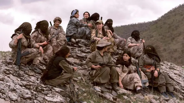 Combatientes kurdas con sus armas sentadas en la cima de una colina rocosa.