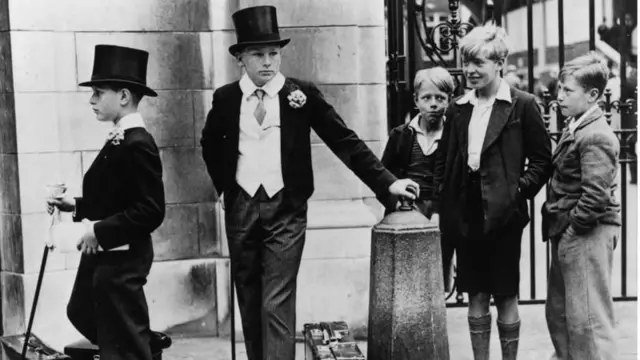 Unos niños con traje de chaqueta y algunos también sombrero de copa en una imagen en blanco y negro.