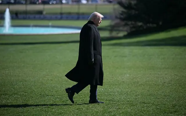 Donald Trump camina por la grama de la Casa Blanca con una gran gabardina negra