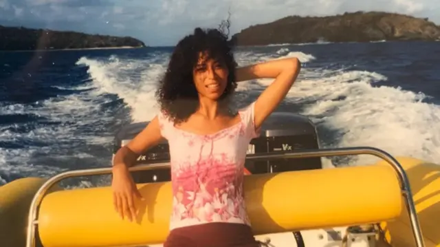 Lisa Phillips en un barco, con una blusa rosa y el brazo izquierdo detrás de la cabeza. La isla de Epstein se ve al fondo.