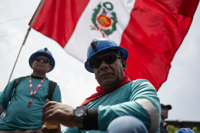 Dos trabajadores bajo una bandera de Perú.