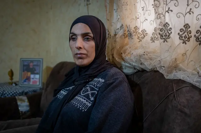 Primer plano de la madre de Jad, con aspecto desolado, sentada en el salón familiar del campo de refugiados de al-Far'a, en la Cisjordania ocupada. Detrás de ella, sobre la mesa, hay una foto enmarcada de Jad.