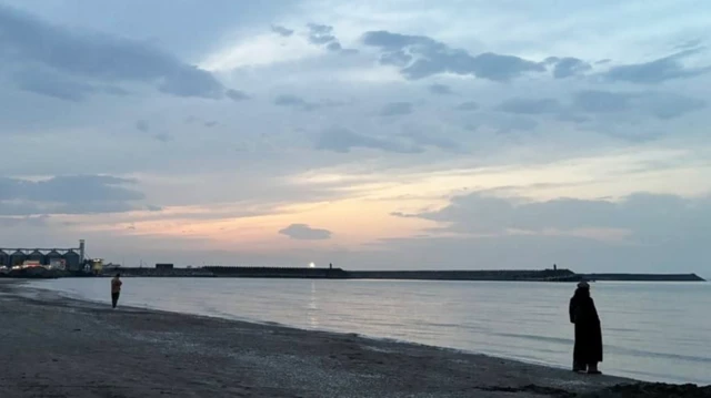 Dos personas, una distante de la otra, están paradas en la playa en la costa del mar Caspio