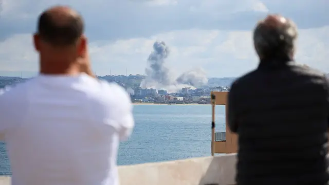 Dos personas, de espaldas a la cámara, contemplan el perfil urbano de Tiro mientras una columna de humo se eleva sobre la ciudad este miércoles.