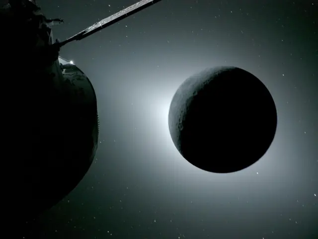 La Luna, vista aquí a contraluz del Sol durante un eclipse solar el 6 de abril de 2026, fue fotografiada por una de las cámaras situadas en las alas del panel solar de la nave Orion. Orion es visible en primer plano, a la izquierda. La Tierra refleja la luz solar en el borde izquierdo de la Luna, que aparece ligeramente más brillante que el resto del disco. El punto brillante visible justo debajo del borde inferior derecho de la Luna es Saturno. Más allá, el punto brillante en el borde derecho de la imagen es Marte.