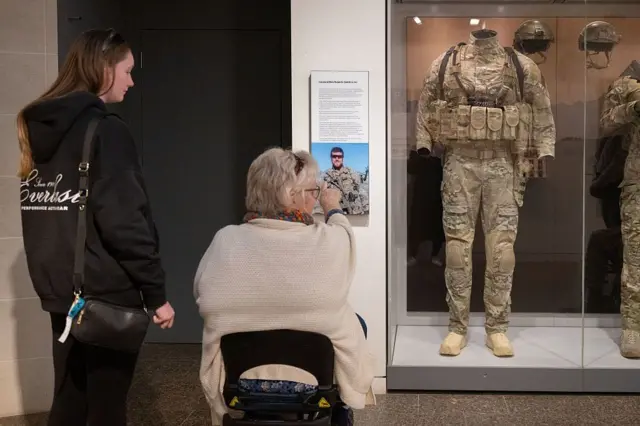 Una señora en silla de ruedas junto a otra más joven ven uno de los uniformes de Roberts-Smith en el Museo de la Guerra de Australia.