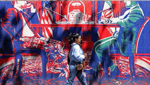 Una mujer pasa frente a un mural antinorteamericano de colores vivos que representa las conversaciones entre Irán y Estados Unidos.