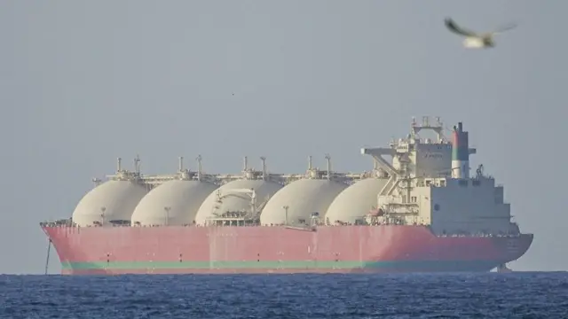 Un gigantesco buque cisterna rojo, con cinco enormes cúpulas blancas, se aleja de la cámara.