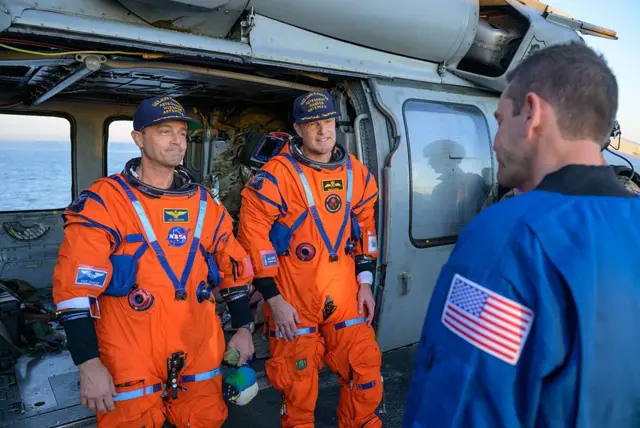 El comandante Reid Wiseman (izq.) y astronauta Jeremy Hansen son recibidos por el administrador de la NASA, Jared Isaacman, a borto del John P. Murtha.