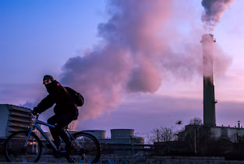 Un hombre pasea en bicicleta junto a las emisiones de una torre de refrigeración. (Georgi Licovski/EFE)
