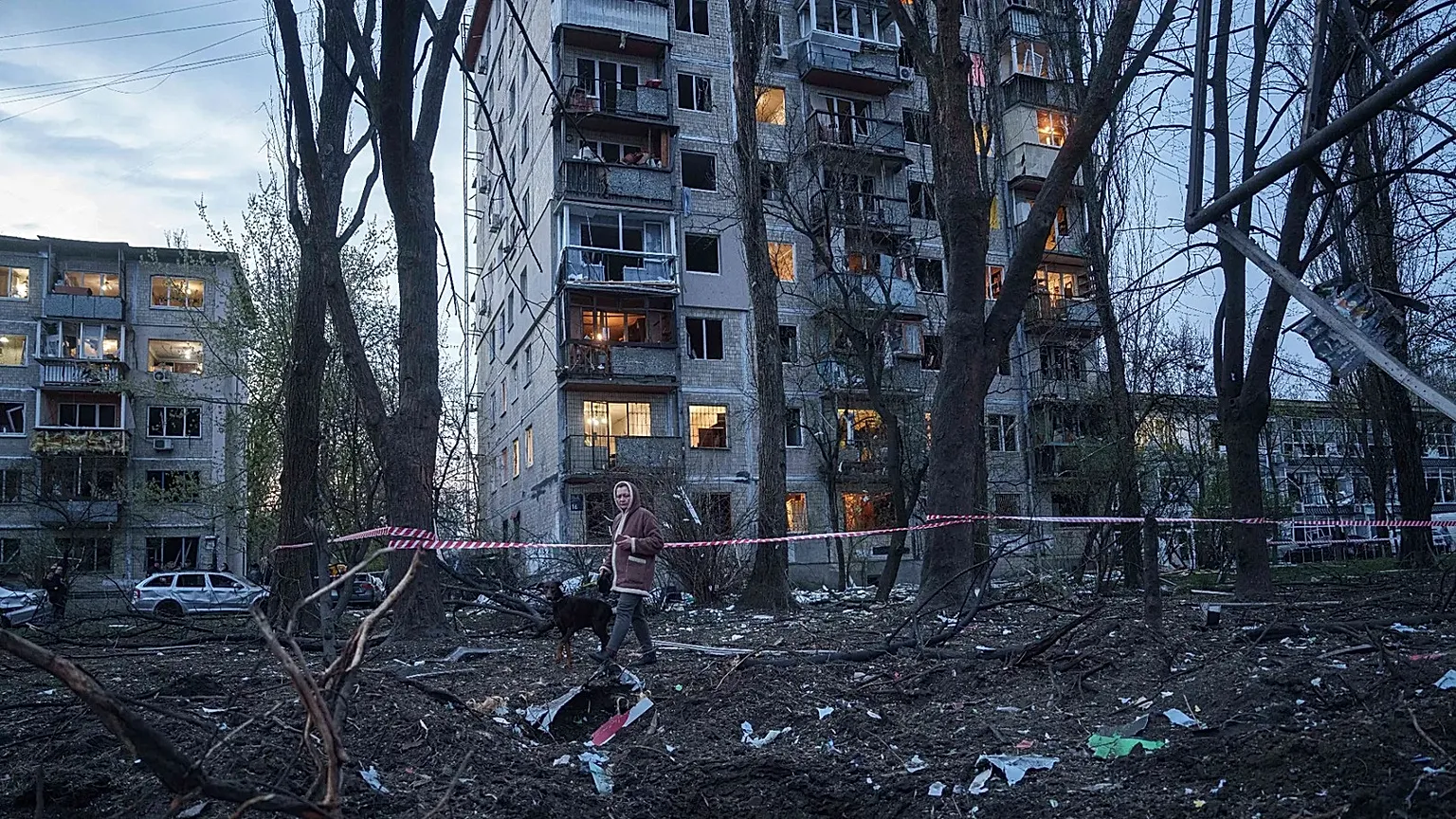 A woman with a dog walks among the rubble of a house damaged after a Russian strike on residential area in Kyiv, Ukraine, on Thursday, April 16, 2026.