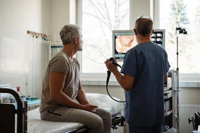 Un doctor le enseña una colonoscopia en una pantalla a un paciente.