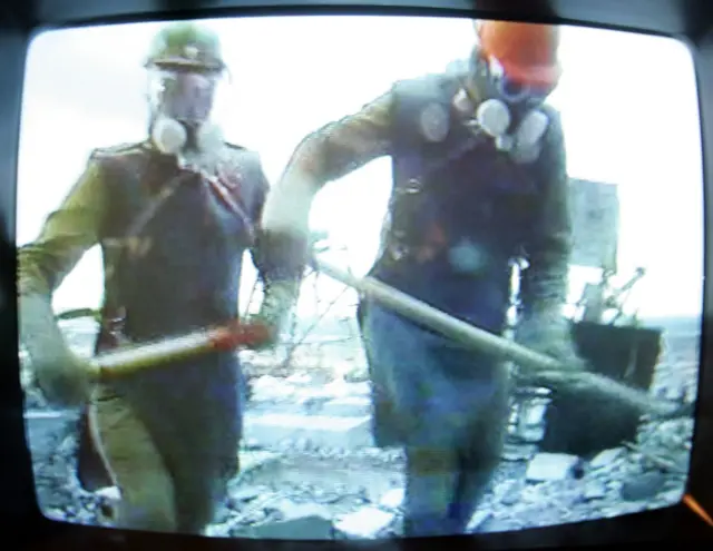 En el museo de Chernóbil, en Kyiv, un televisor muestra un documental sobre los liquidadores. Enmarcada por los bordes negros de un televisor antiguo, la imagen muestra a dos hombres con delantales de plomo, cascos de obra y máscaras respiratorias, cargando palas.