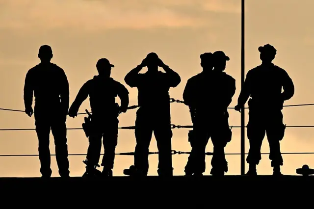 Siluetas de seis militares a contraluz en la cubierta de un barco de guerra estadounidense.
