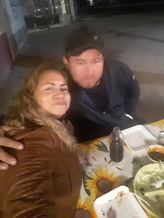 Ceci Flores a la izquierda, con chaqueta marrón, sentada a la mesa junto a su hijo Marco Antonio, que lleva una gorra y la abraza con el brazo derecho.