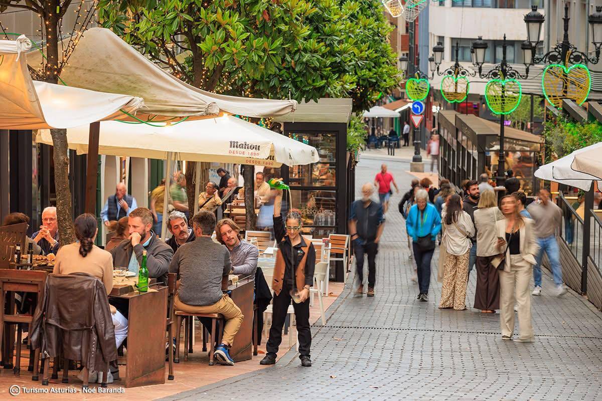 Foto: Una camarera escancia sidra en una terraza de esta emblemática calle asturiana. (Turismo Asturias/Noé Baranda)
