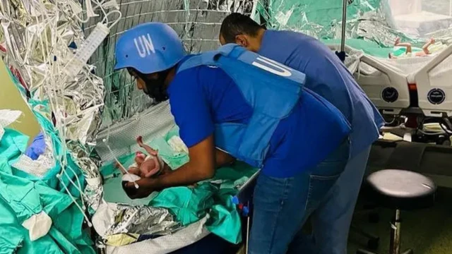 Una mujer con un casco azul de la ONU y un chaleco antibalas sostiene a un bebé diminuto.