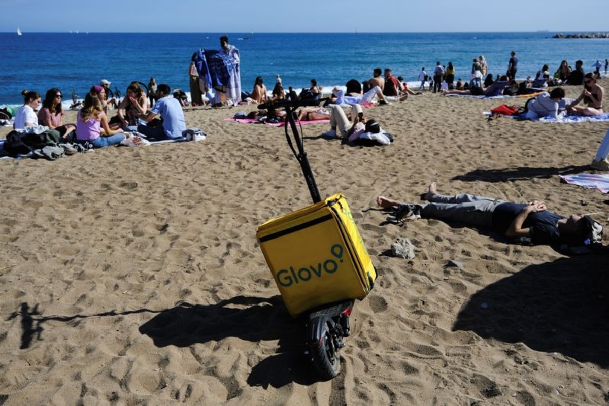 Una mochila de entrega de alimentos de Glovo sobre un patinete eléctrico mientras un repartidor descansa cerca. (REUTERS/Nacho Doce)
