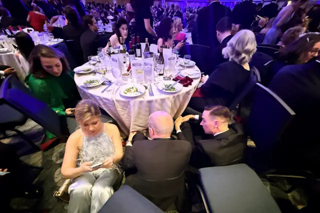 Personas vestidas con trajes de gala sentadas en el piso del evento.
