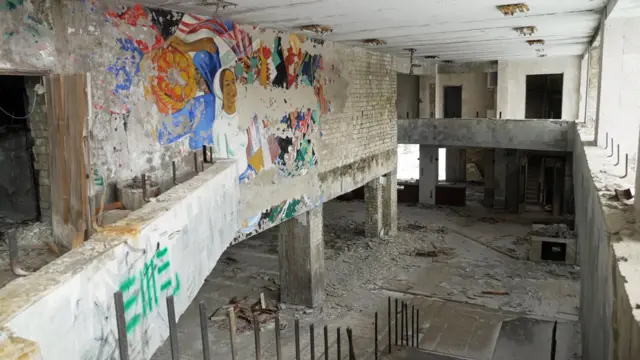 Vista interior del Palacio de la Cultura, en la que se aprecian paredes de ladrillo visto y suelos de hormigón. Queda parte de un colorido mural, y en el suelo hay baldosas sueltas y otros escombros.