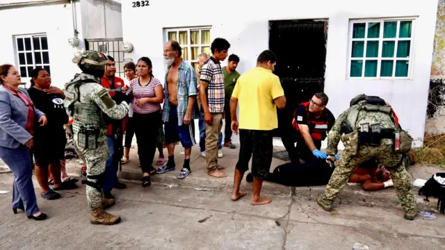 Julio César Vega y Héctor Torres atienden a un hombre tendido en la acera mientras la gente observa. Dos soldados uniformados y con casco también se encuentran en el lugar.