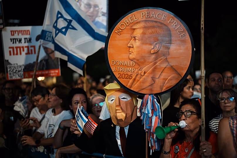 A man wearing a mask resembling US President Donald Trump holds a sign designed like a Nobel Peace Prize medal during a rally in Tel Aviv, 11 October, 2025