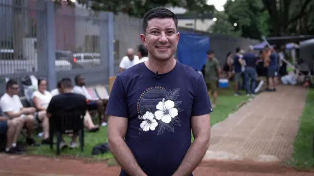 Cornelio Melgarejo, un hombre joven, con una playera azul estampada con flores blancas, está parado frente a una fila de brasileños que buscan solicitar residencia en Paraguay.