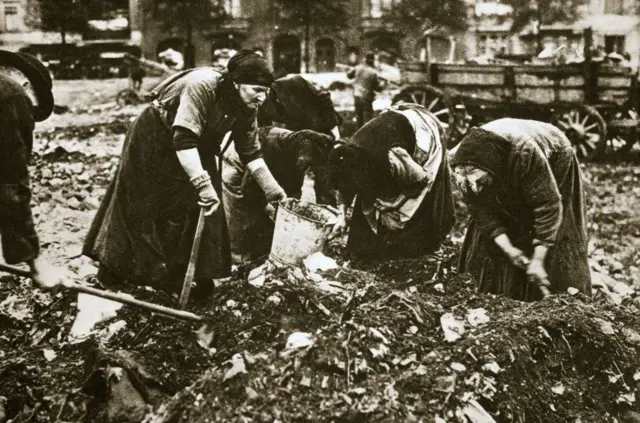 Un grupo de mujeres con cubos y azadas agachadas sobre un montón de basura en una foto de época.