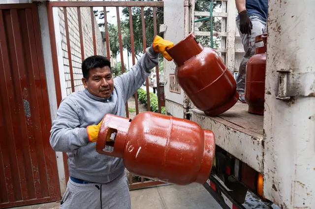 Un hombre descarga dos bombonas de gas de un camión. 