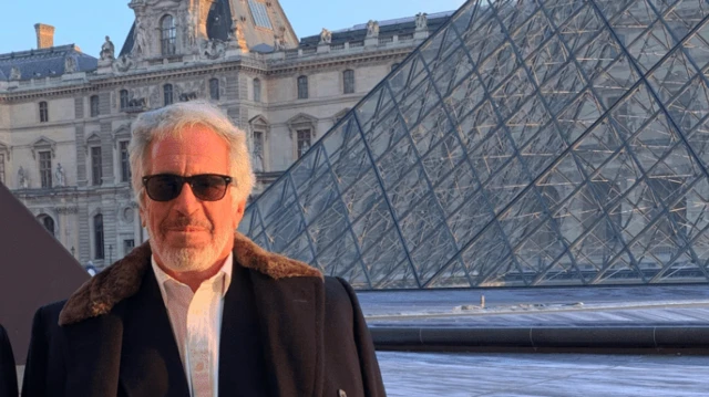 Jeffrey Epstein, con barba gris, abrigo y gafas de sol, posa frente al Museo del Louvre y su pirámide de cristal.