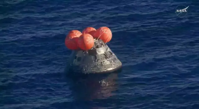 La cápsula Orión despliega cuatro flotadores redondos color naranja mientras yace sobre la superficie del mar