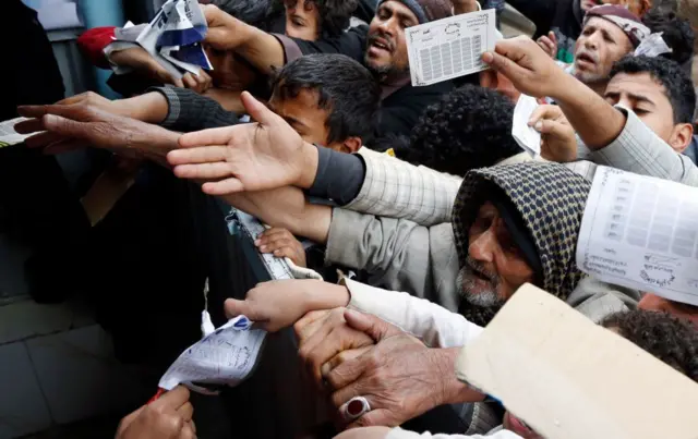 Una multitud se agolpa y estira sus brazos sujetando papeles en Yemen.