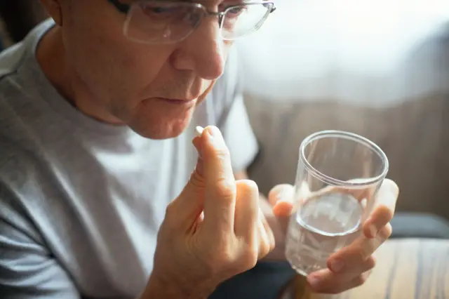 Un señor mayor tomándose una aspirina