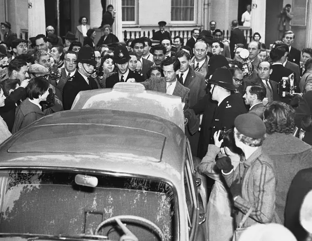 Un hombre abre el baúl de un automóvil, mientras está rodeado por varios policías londinenses y una gran cantidad de periodistas y curiosos tomando fotografías.