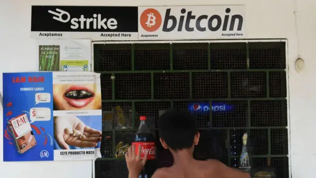 un niño hace unas compras por una ventana en El Salvador. sobre la ventana hay un letrero que dice bitcoin.