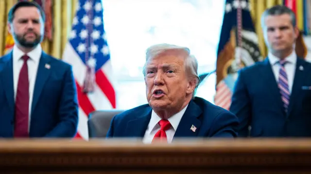 El vicepresidente de EE.UU., JD Vance (izq.), y el secretario de Defensa de EE.UU., Pete Hegseth (der.) parados detrás del presidente Donald Trump, durante la firma de una orden ejecutiva en la Oficinal Oval de la Casa Blanca en Washington