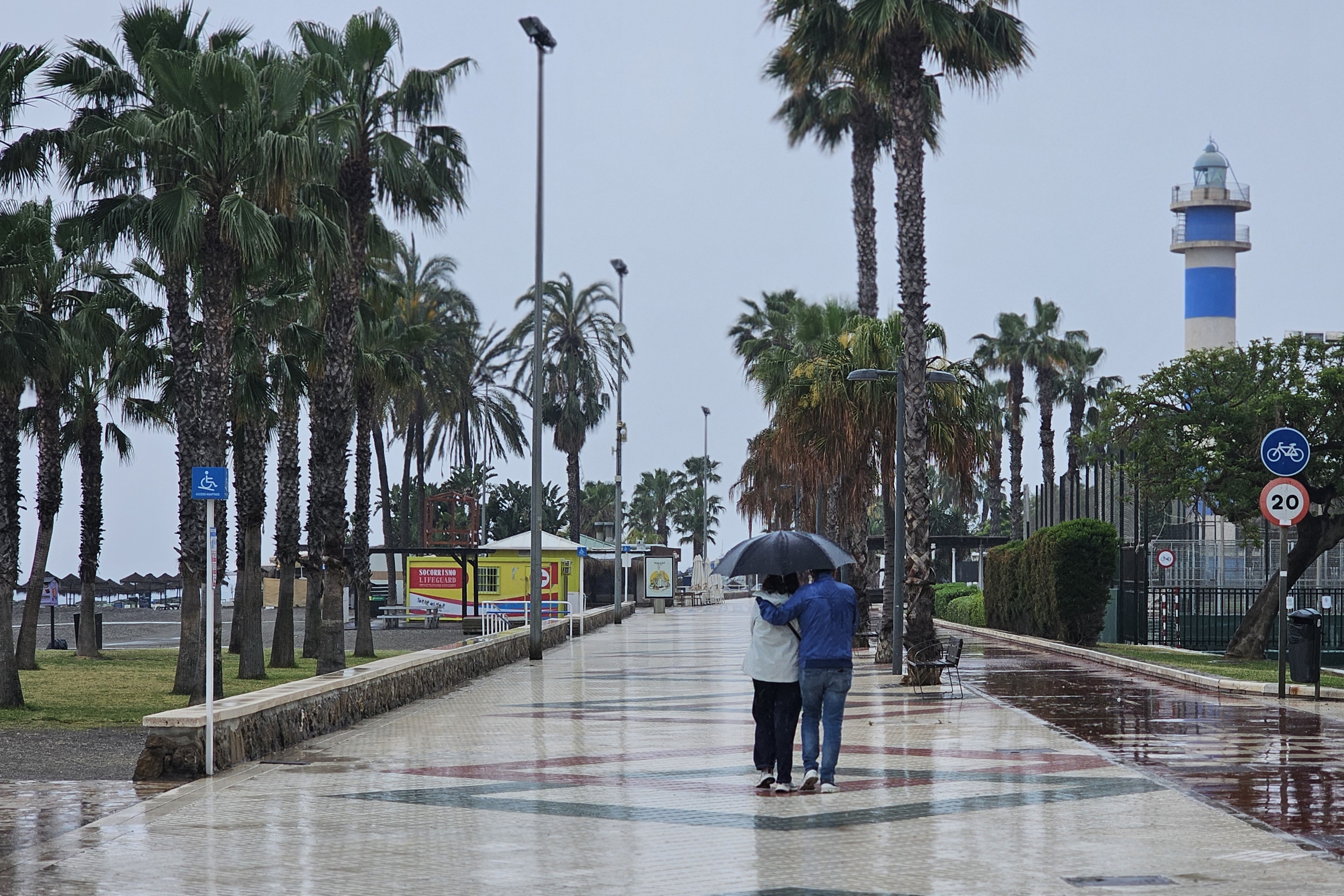 Una pareja pasea bajo la lluvia en un paseo marítimo.