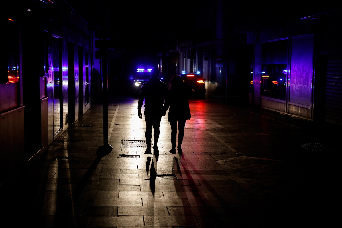 Dos personas caminan por una calle comercial sin iluminación eléctrica mientras los coches de policía patrullan en Ronda, España, el 28 de abril de 2025. (REUTERS/Jon Nazca)