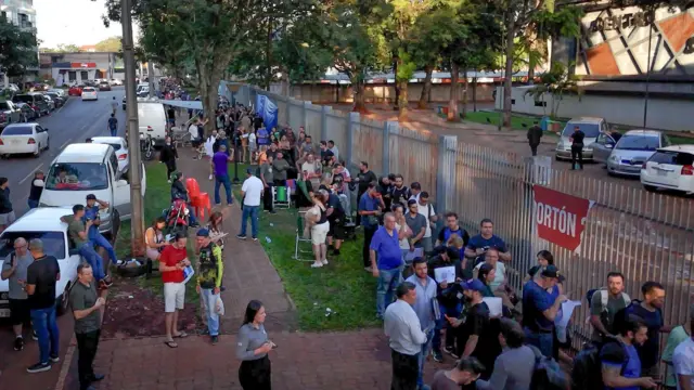 Vista aérea de una larga fila de personas frente a un edificio público.