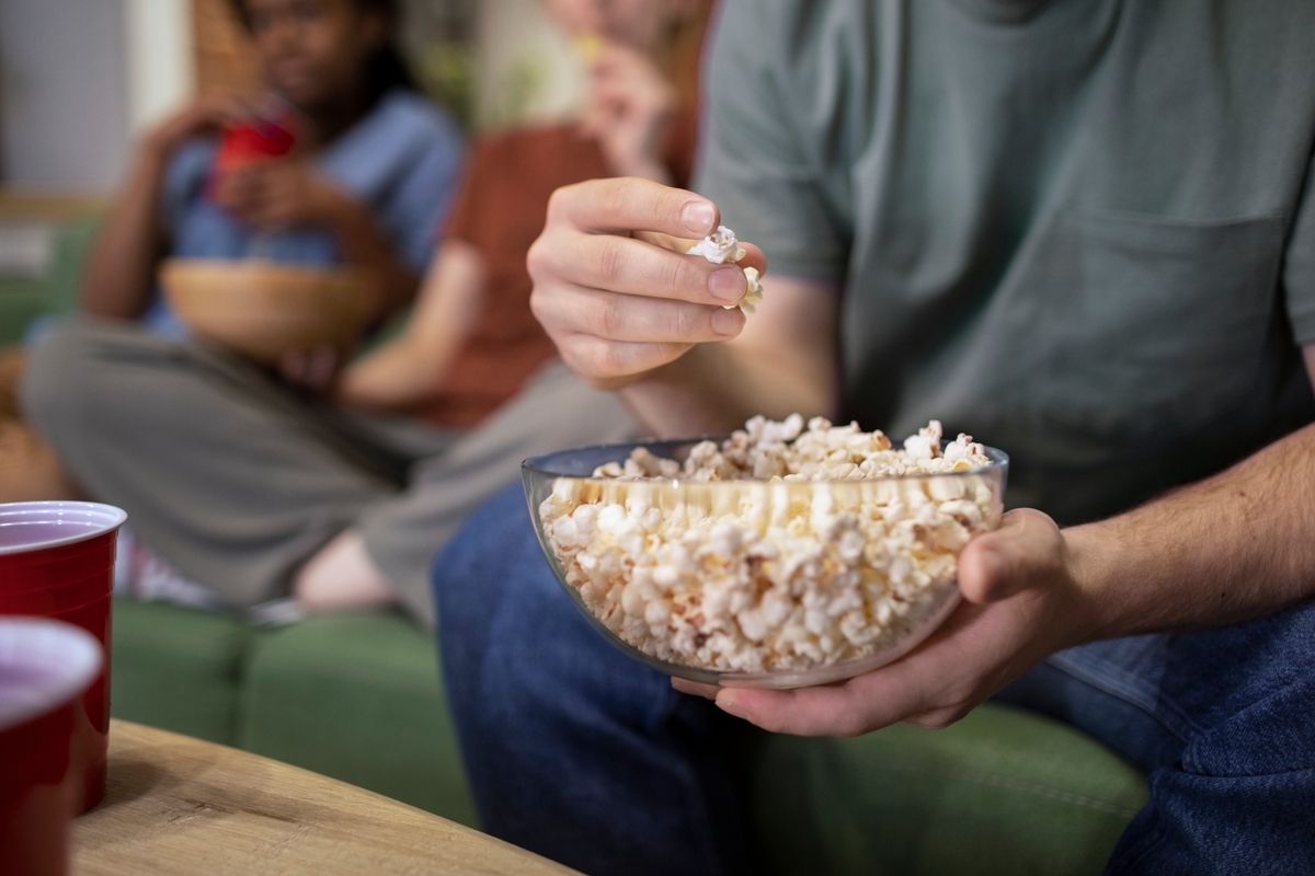 Tres personas comiendo palomitas en el sofá. Una de ellas está en primer plano. No se les ve las caras