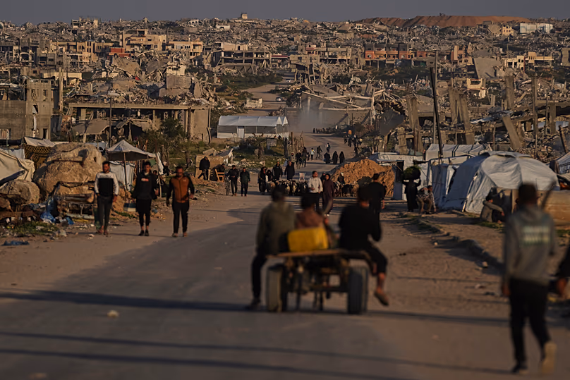 Palestinians walk along a street surrounded by buildings destroyed during Israeli air and ground operations in Khan Younis, 9 April, 2026