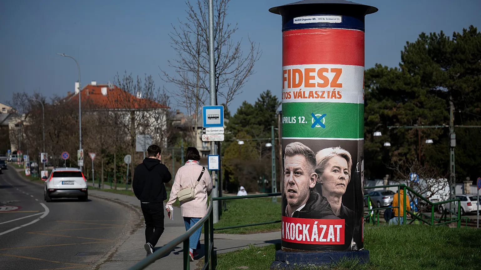 People walk next to a campaign poster which reads, "They're a risk. Fidesz is the safe choice" in Budapest, Hungary, on Saturday, March 14, 2026, ahead of the April 12 parliam