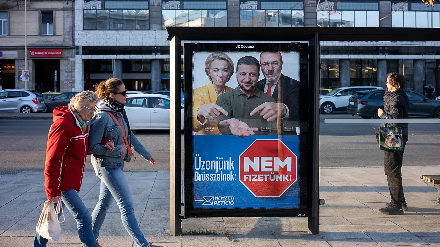 People walk next to a campaign poster which reads, "Our message to Brussels: We won't pay" in Budapest, Hungary, on Saturday, March 14, 2026, ahead of the April 12 parliamenta